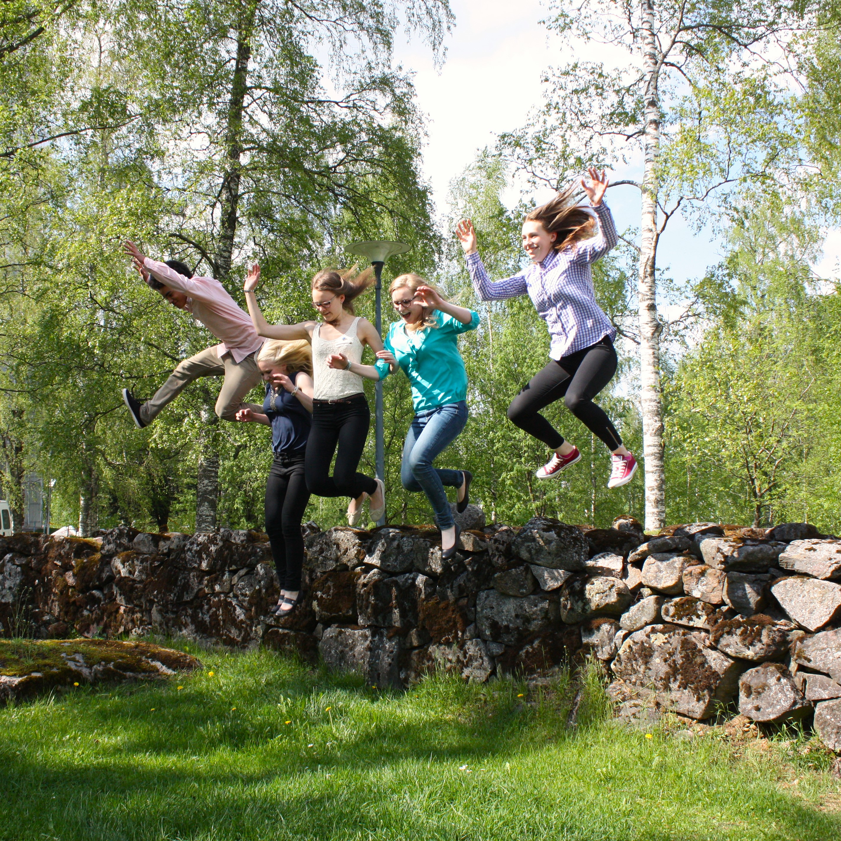 Viisi nuorta hyppää ilmaan kivimuurilta.